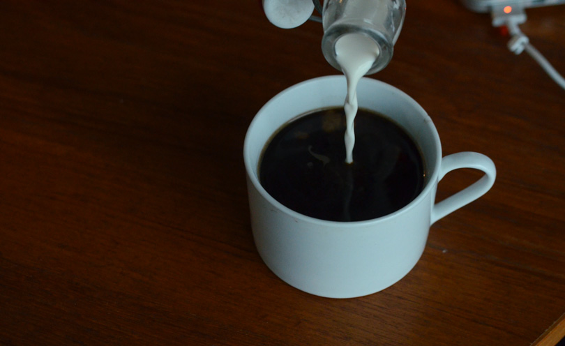 Pouring homemade almond milk made in a Vitamix into black coffee.